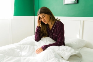 ágyban ülő nő fogja a fejét 